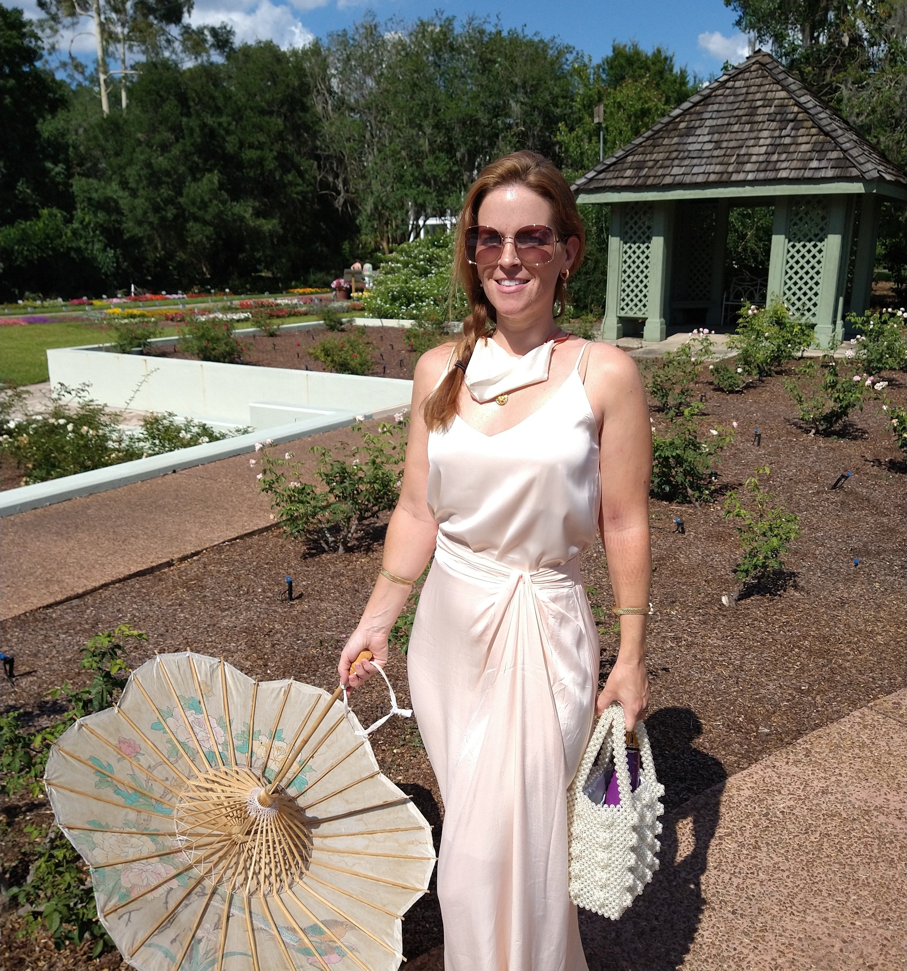 a reviewer wearing the off white silky cami with a silk skirt and a parasol while outside