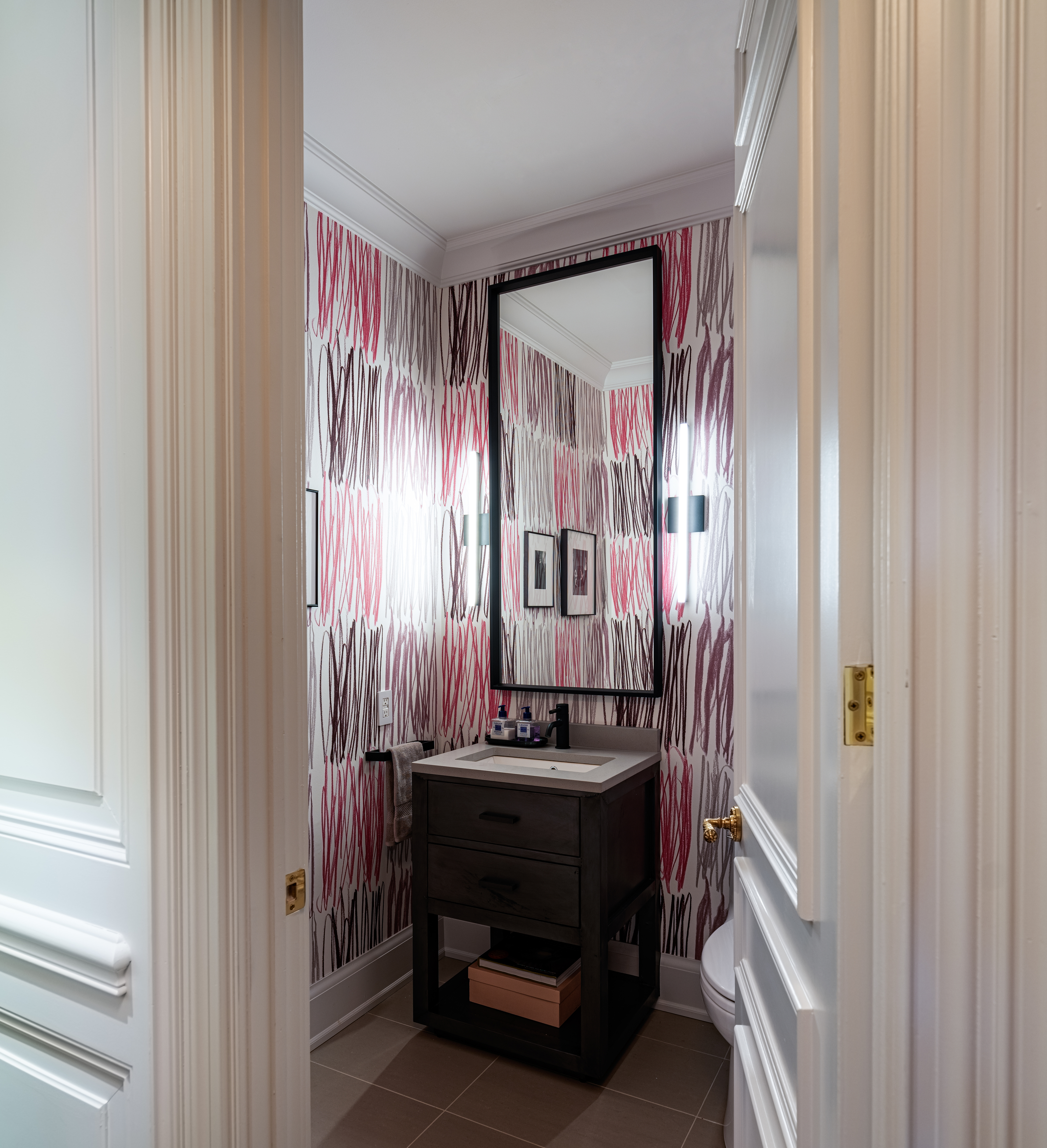 A modern bathroom with a patterned wallpaper, vanity cabinet, and large mirror