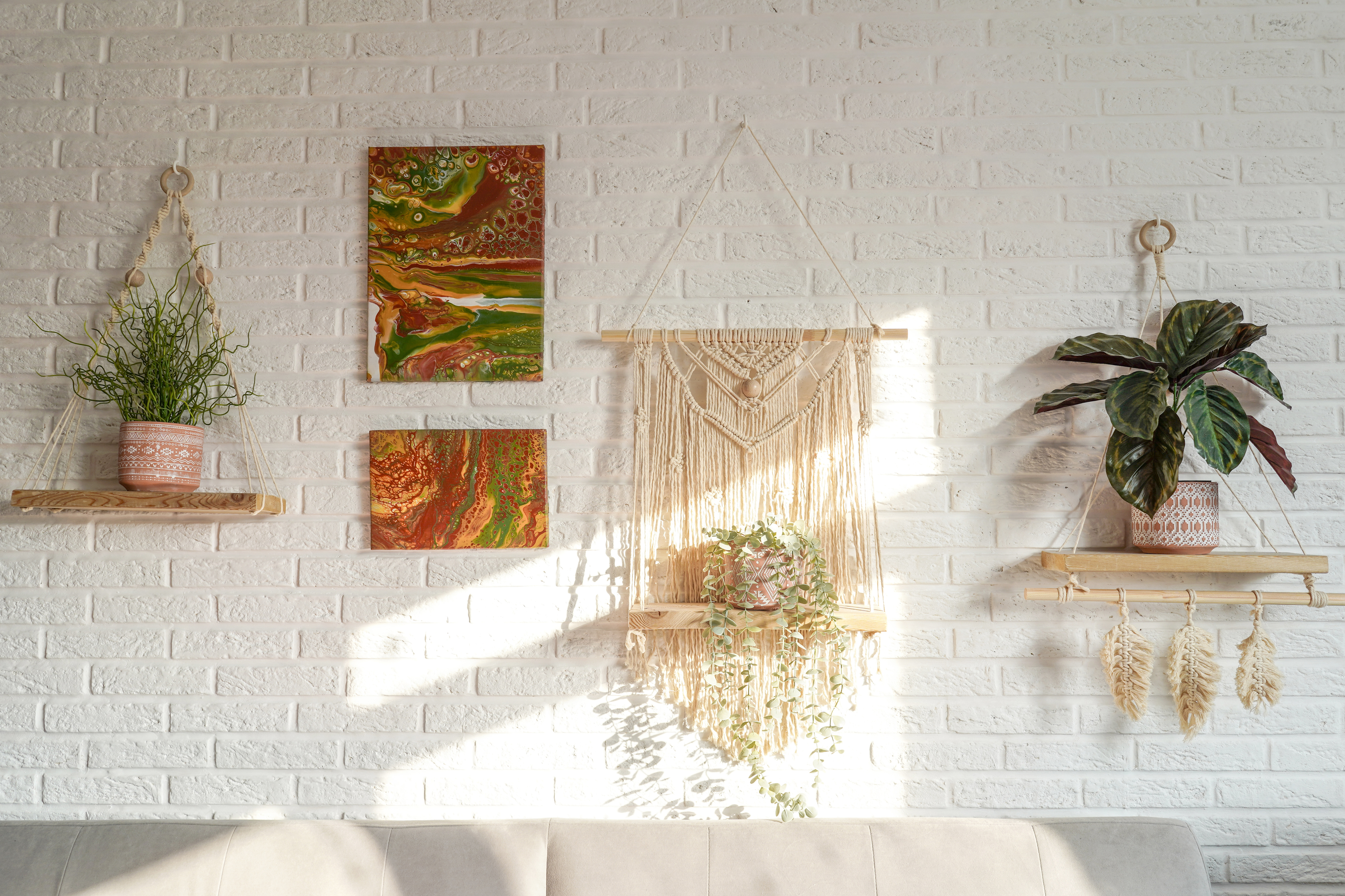 Wall with artistic decor and plants above a sofa, featuring a macramé wall hanging and two paintings