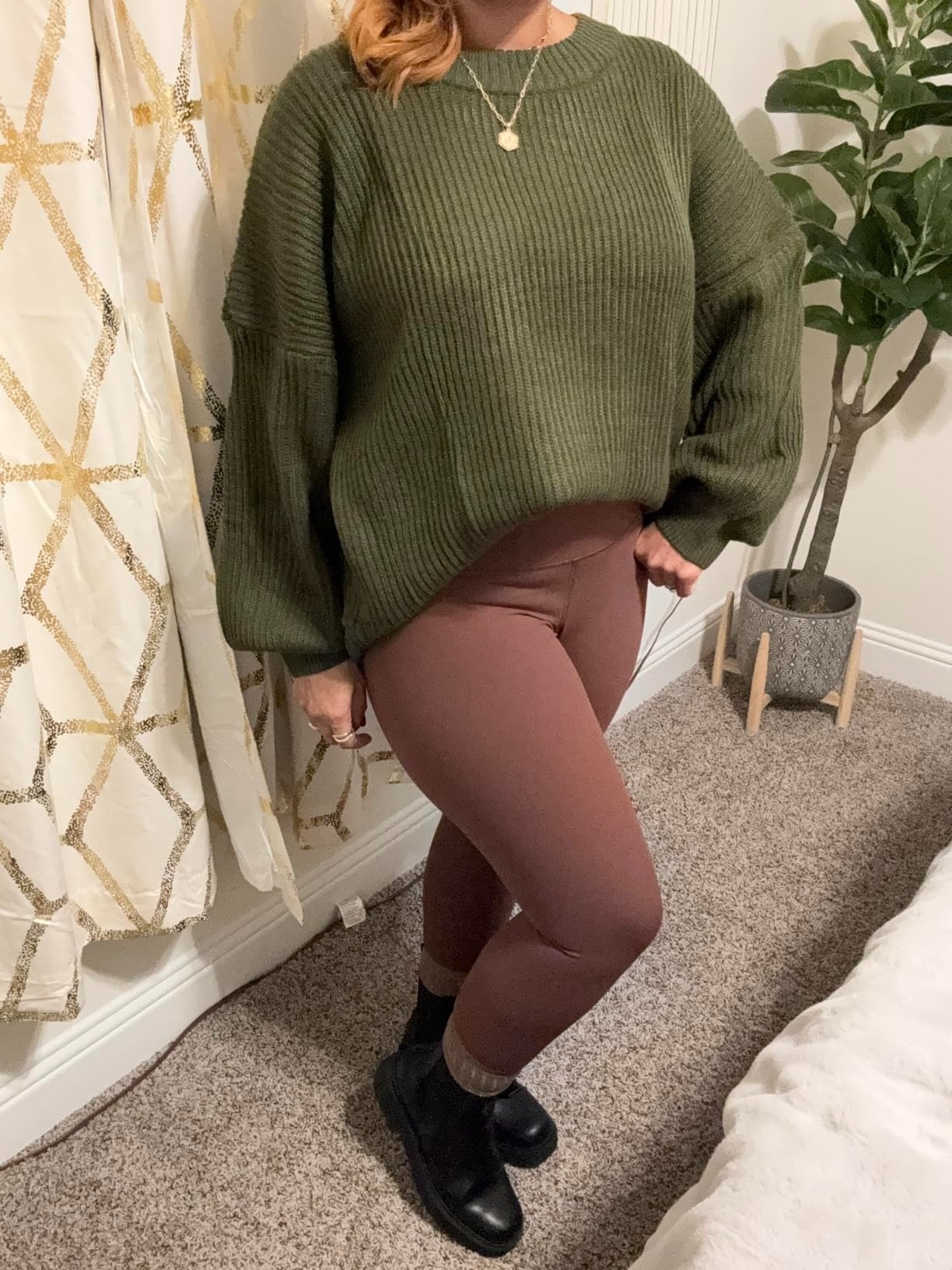 a reviewer in oversized green sweater and brown leggings, paired with black ankle boots, standing indoors