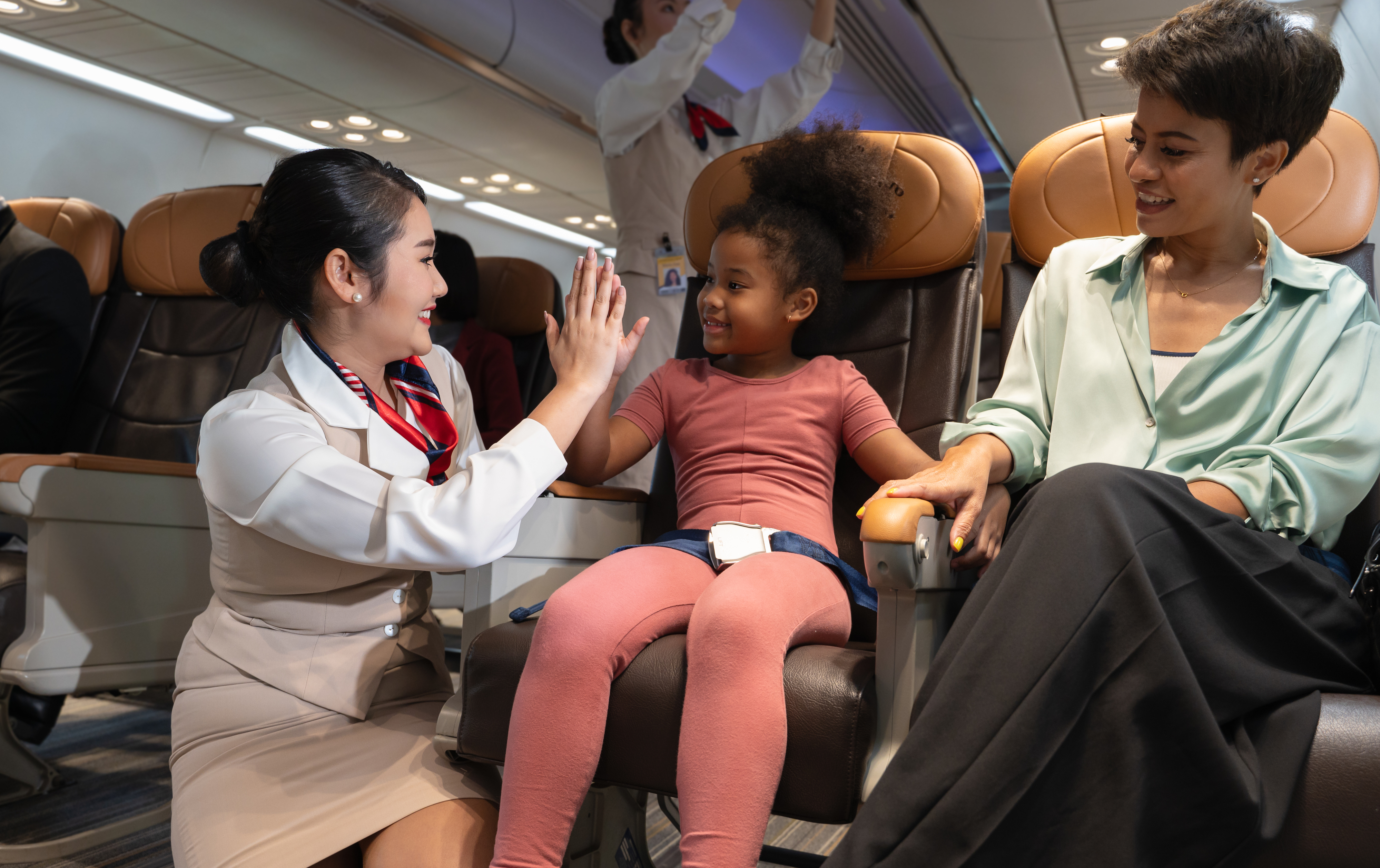 Flight attendant giving high-five to a smiling child seated next to her guardian on a plane