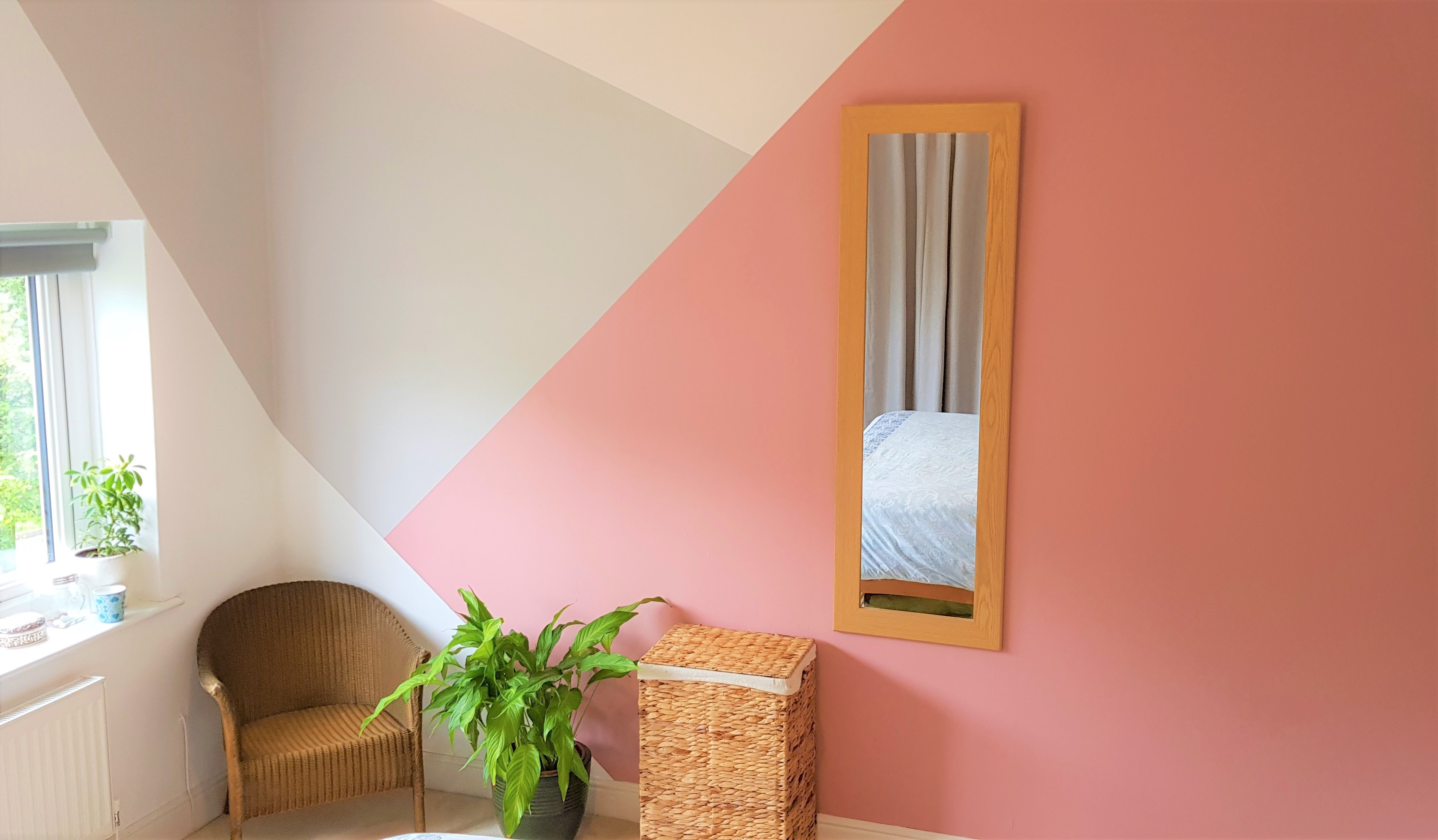 A stylish interior with geometric wall patterns, a mirror, a wicker chair, and a potted plant