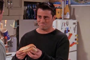 Joey from Friends holding a sandwich and smiling