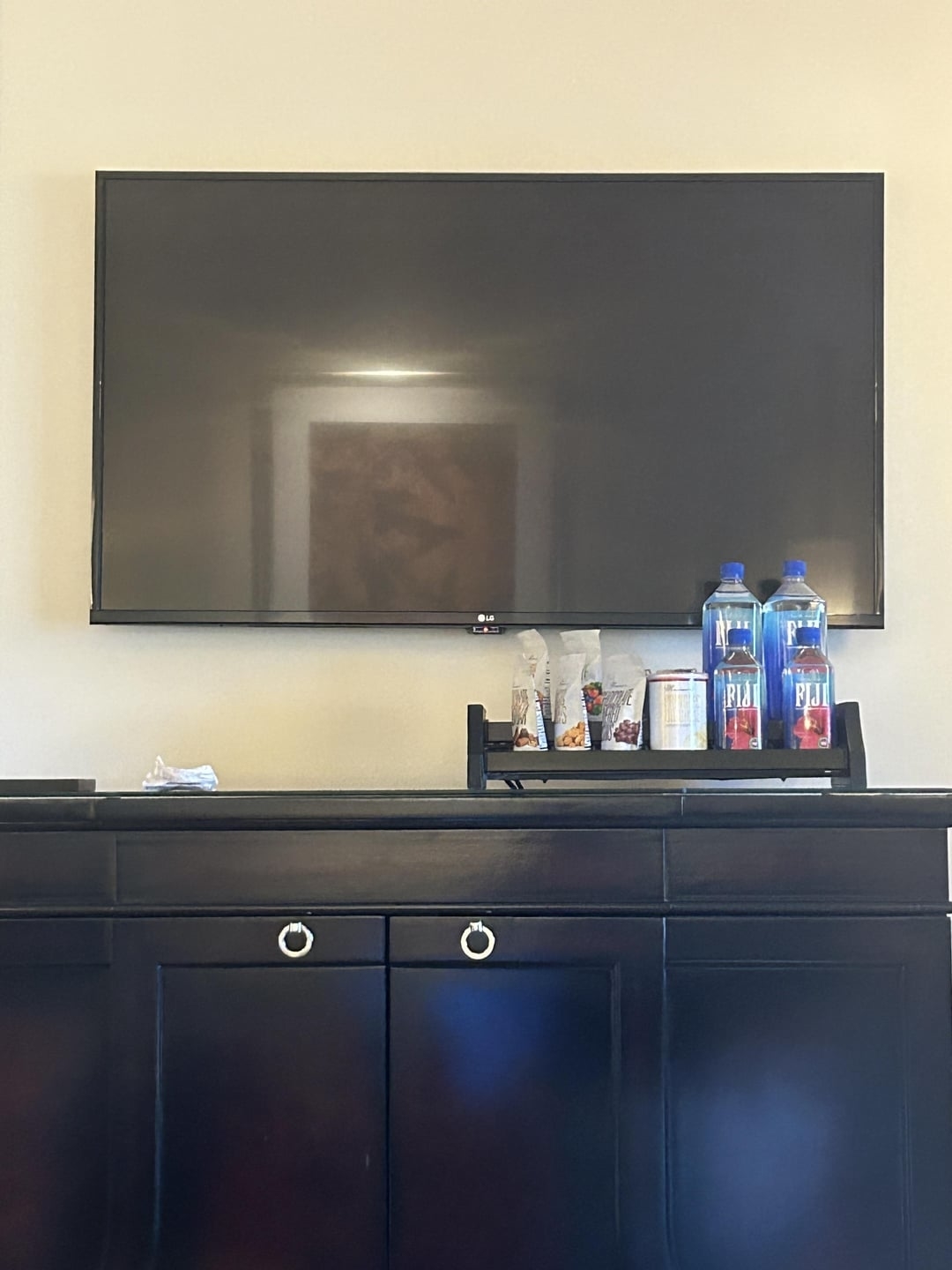 Flat-screen TV mounted on a wall above a cabinet with various items on top, including bottles and snacks