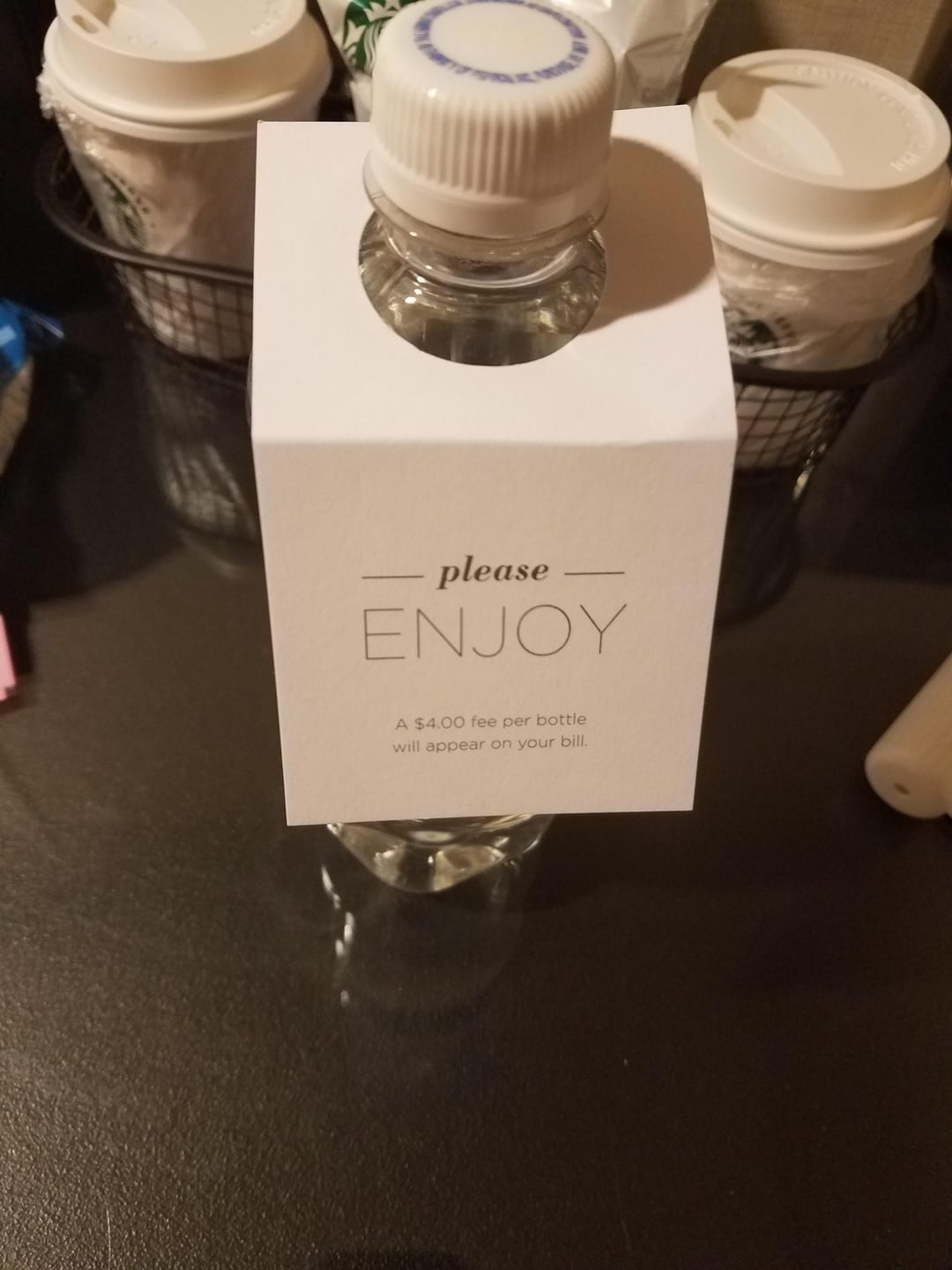 A hotel water bottle with a tag reading &quot;please ENJOY - A $4.00 fee per bottle will appear on your bill.&quot;