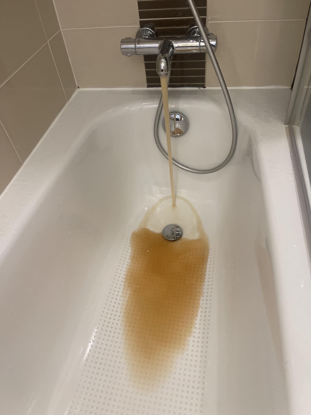 A bathtub with brownish water flowing from the tap, possibly indicating rusty pipes