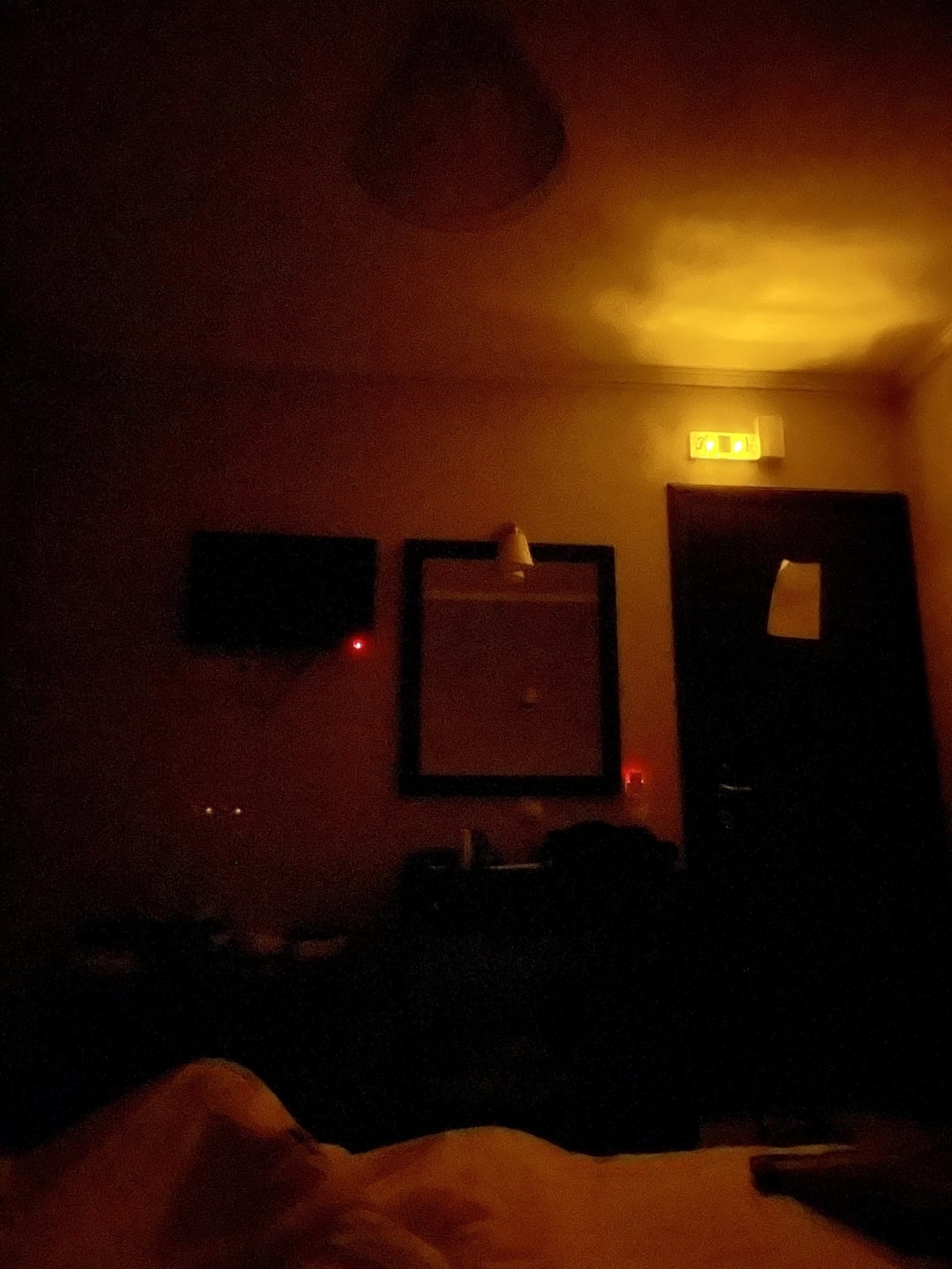 A dark room with faint illumination near the ceiling and a barely visible door