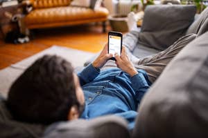 Person lying on a couch using a smartphone, viewed over the shoulder