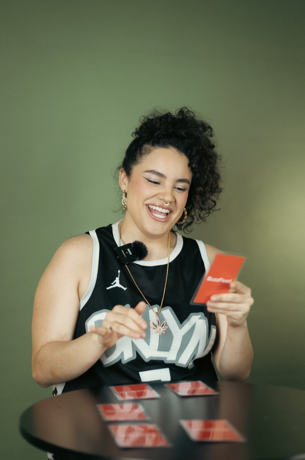 Mujer sonriendo mirando una tarjeta roja, con camiseta sin mangas y micrófono en pecho