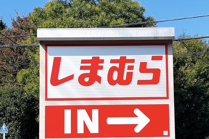駐車場入口の看板に「しまむら IN→」と書かれています。