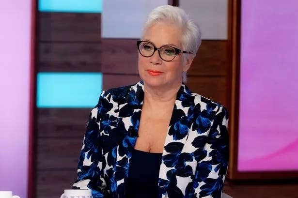 Woman with glasses wearing a floral blazer seated at a desk