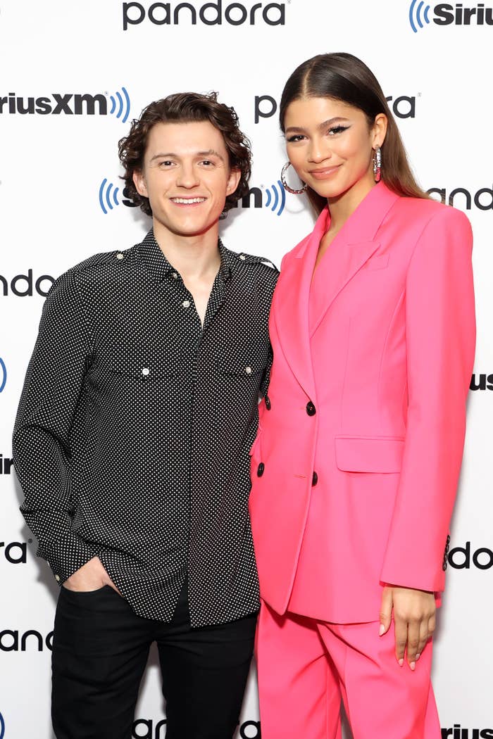 Tom Holland in a patterned shirt and Zendaya in a pink suit pose together smiling