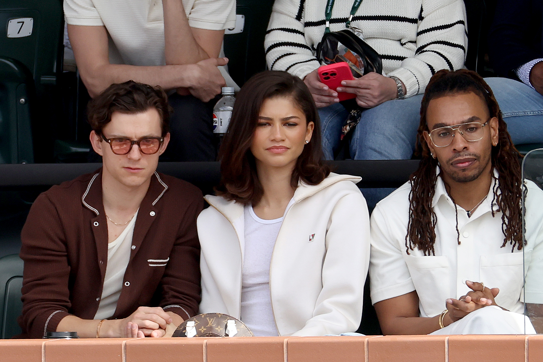 Tom Holland, Zendaya, and another man seated together at an event, dressed in casual attire