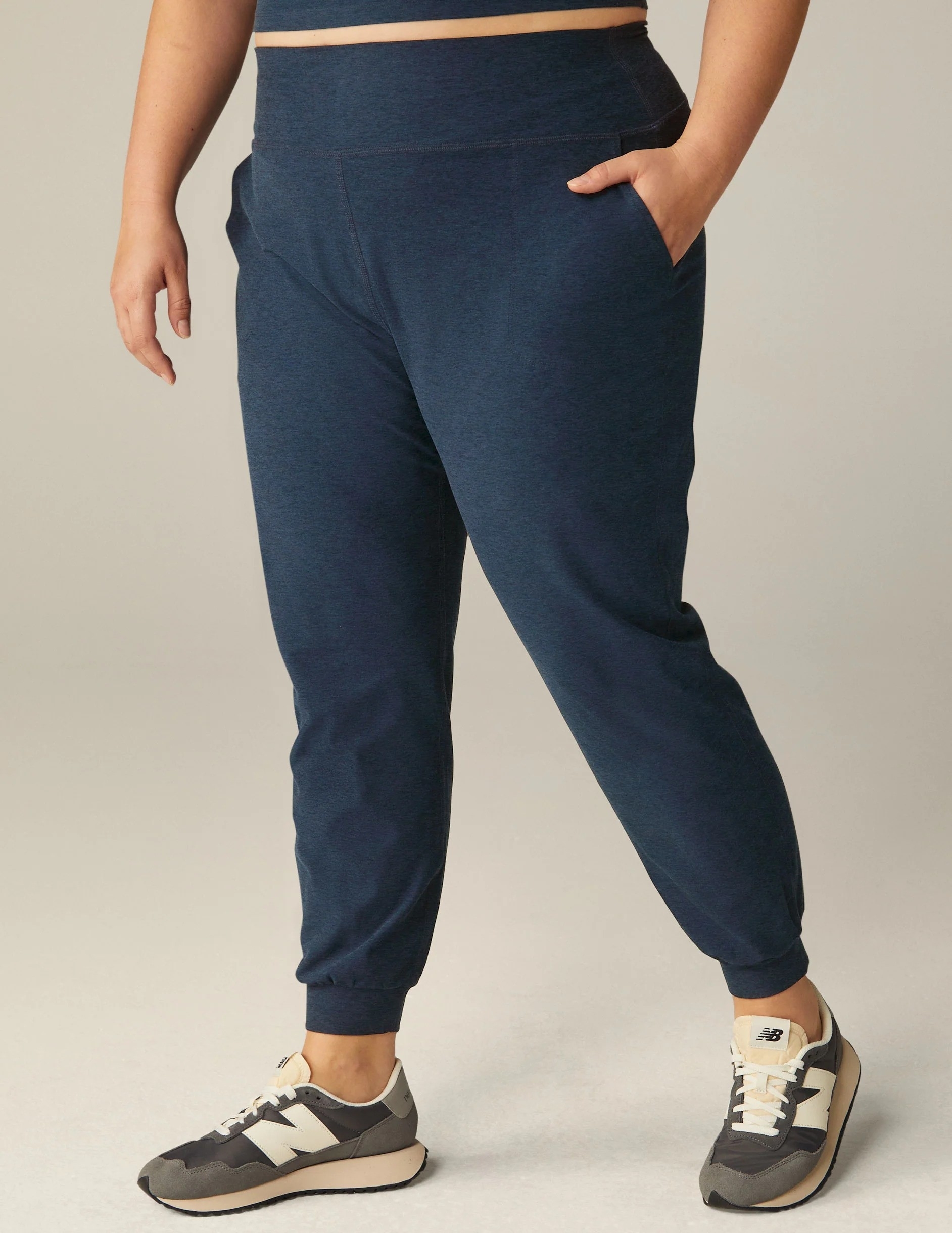 A person standing, wearing navy blue joggers and multicolored sneakers, focus on the lower half of the body