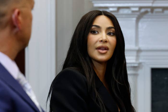 Kim Kardashian, wearing a black outfit, speaks during an event, with a partial view of a man&#x27;s profile in the foreground