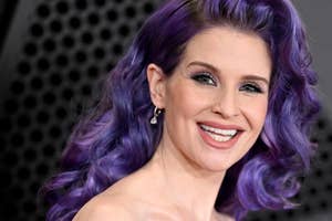 Smiling woman with purple hair styled in waves, elegant earrings, makeup, at a celebrity event