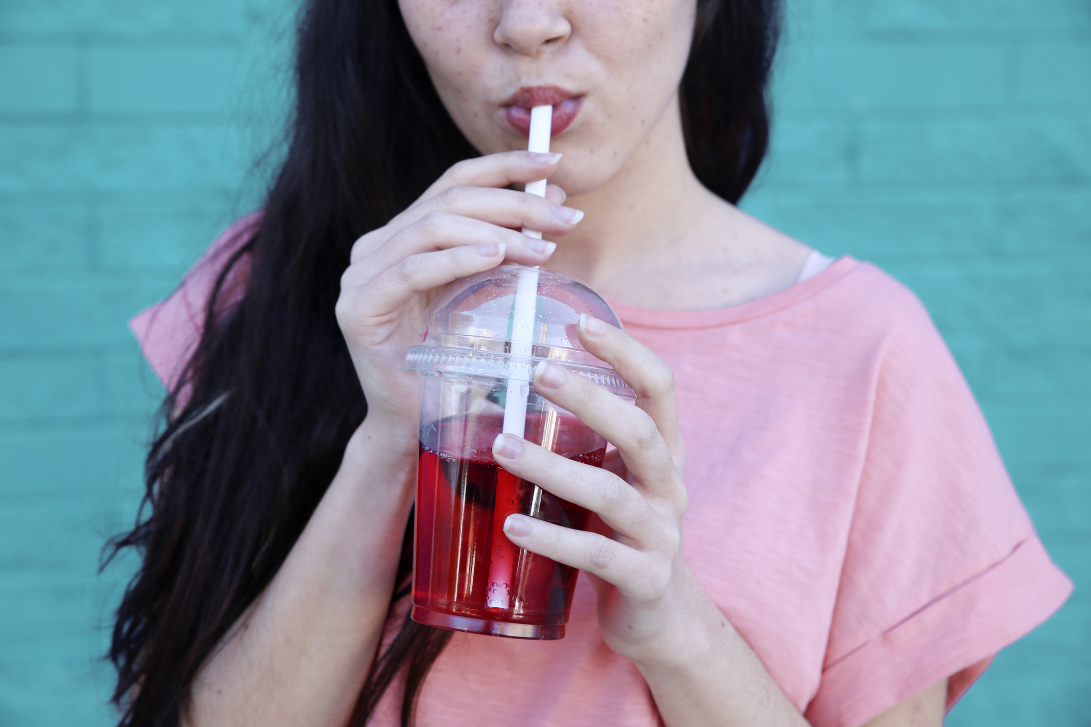 Person sipping a drink through a straw wearing a casual top