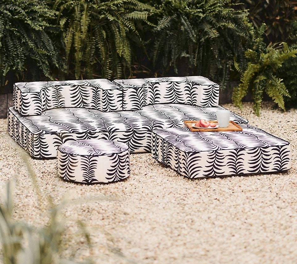Outdoor seating arrangement with patterned cushions and a central table with items on it, set against plants. Perfect for patio shopping inspiration