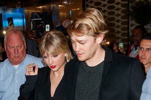 Taylor Swift in a sequined outfit and Joe Alwyn in a black coat walk together among paparazzi