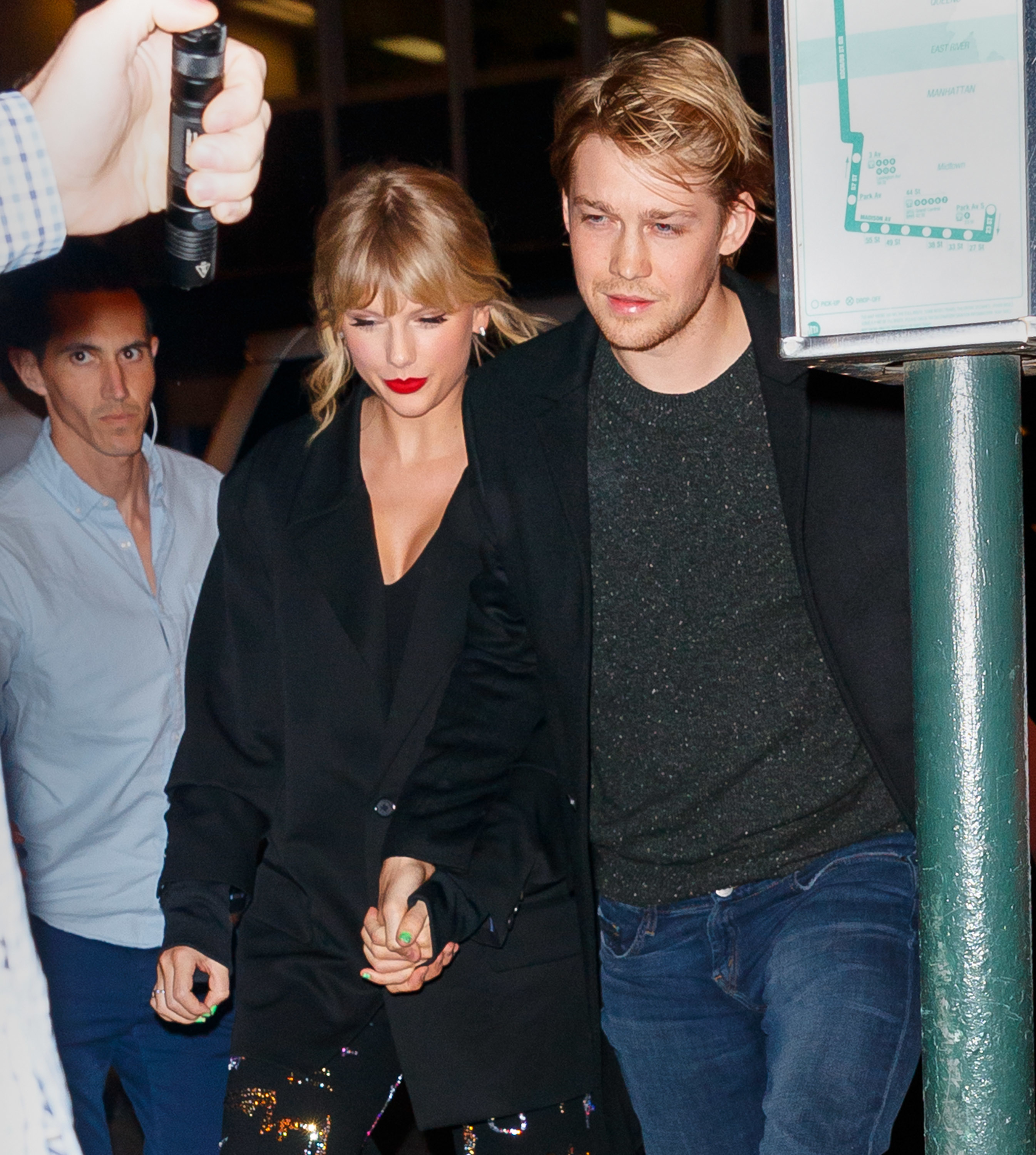 Taylor Swift and Joe Alwyn walking together, Taylor in a black jacket with sparkly accents