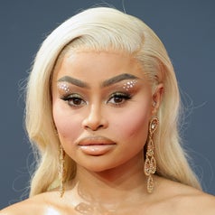 Close-up of Blac Chyna with decorative makeup and statement earrings, wearing a gold chest piece