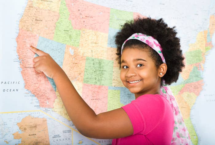 Young girl pointing at a map, smiling at the camera
