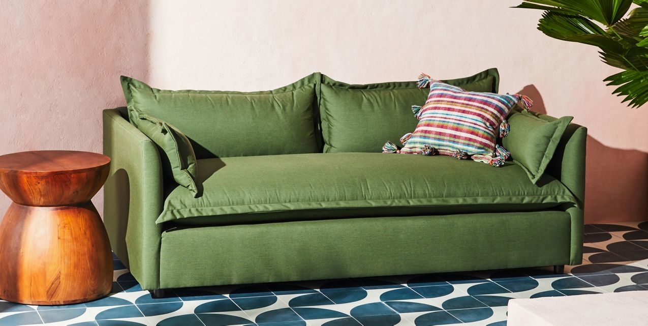 Green sofa with a striped cushion on it, beside a wooden stool on a patterned floor