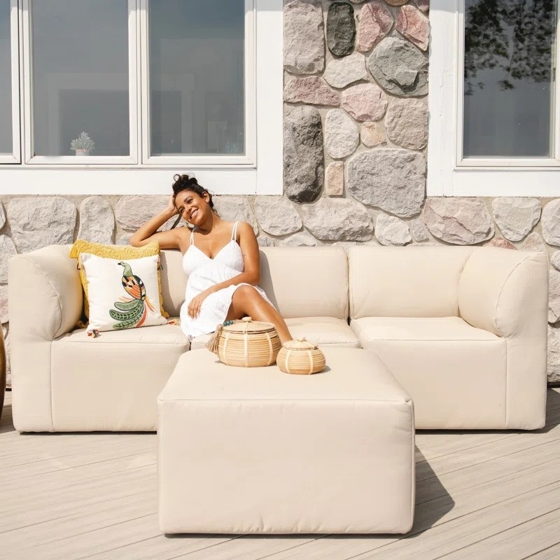 Woman reclining on an outdoor sofa with cushions, wearing a white dress, next to handbags
