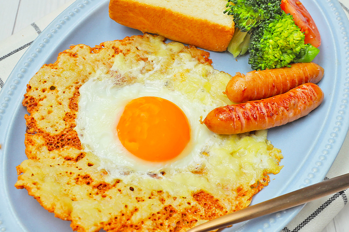 朝食の盛り合わせ、目玉焼き、トースト、ブロッコリーとトマト、チーズソーセージが含まれています。