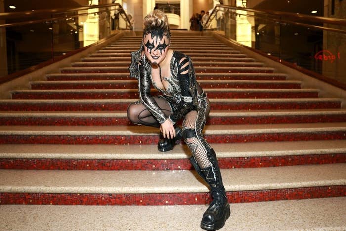 Woman poses connected  stairs, successful  a sparkly jumpsuit with cutouts, mask, fishnet details, and level    boots