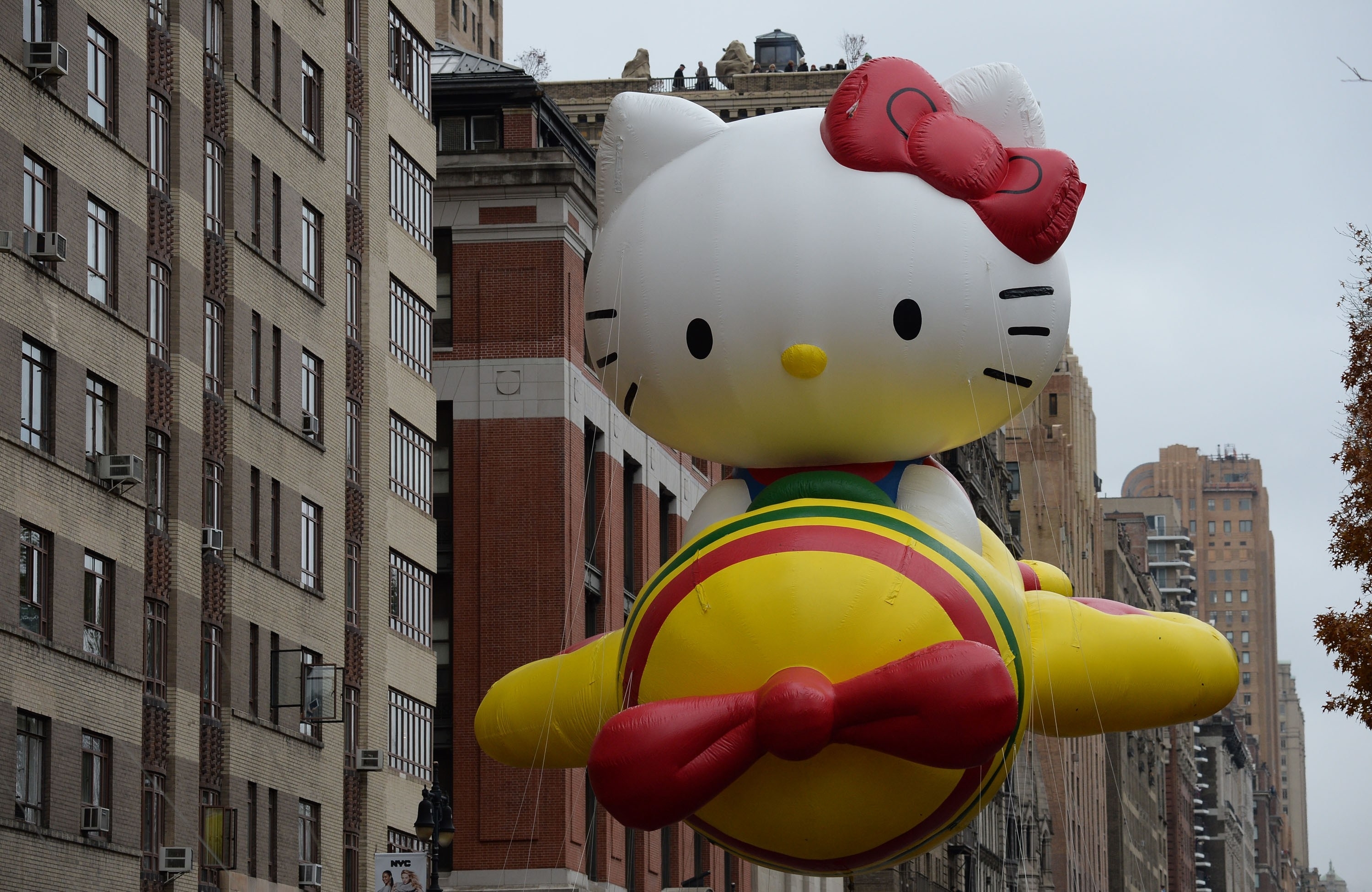Hello Kitty balloon floats in a parade with city buildings in the background