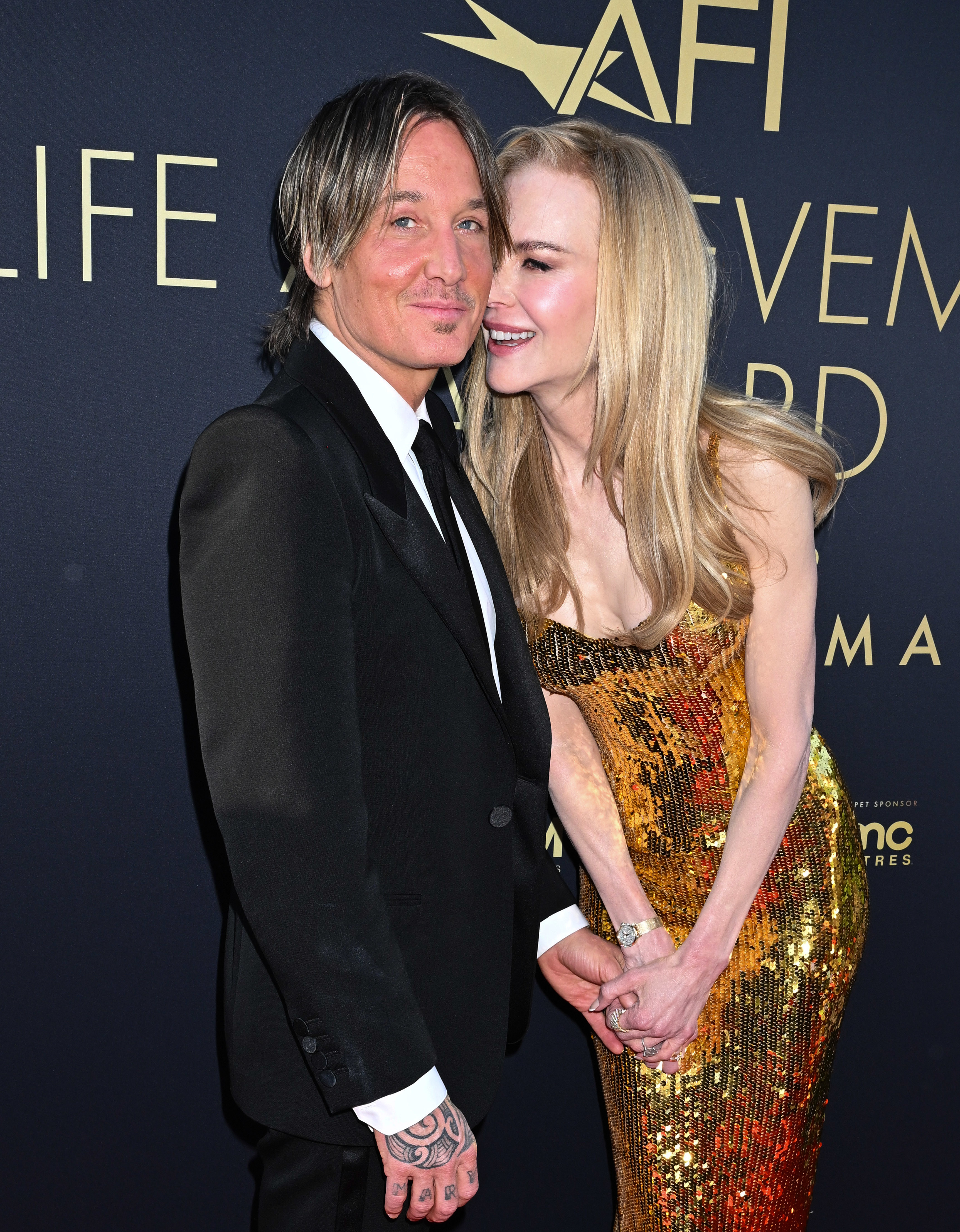 Keith Urban in a black suit with Nicole Kidman in a sequined dress, both smiling at an event