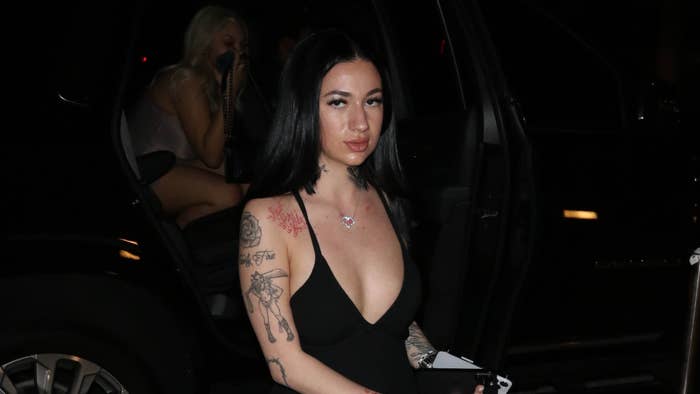 Person in a deep-cut black ensemble exiting a vehicle, tattoos visible, at a night event