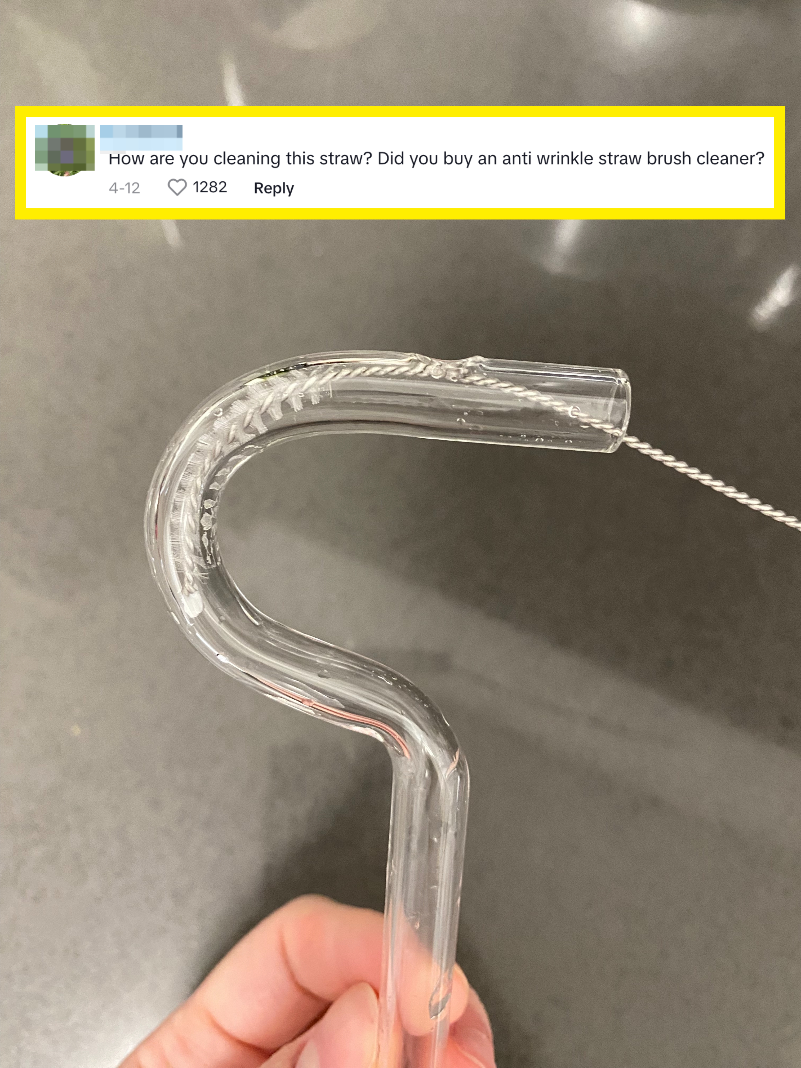 Close-up of a hand holding a glass anti-wrinkle straw with a straw brush stuck in it