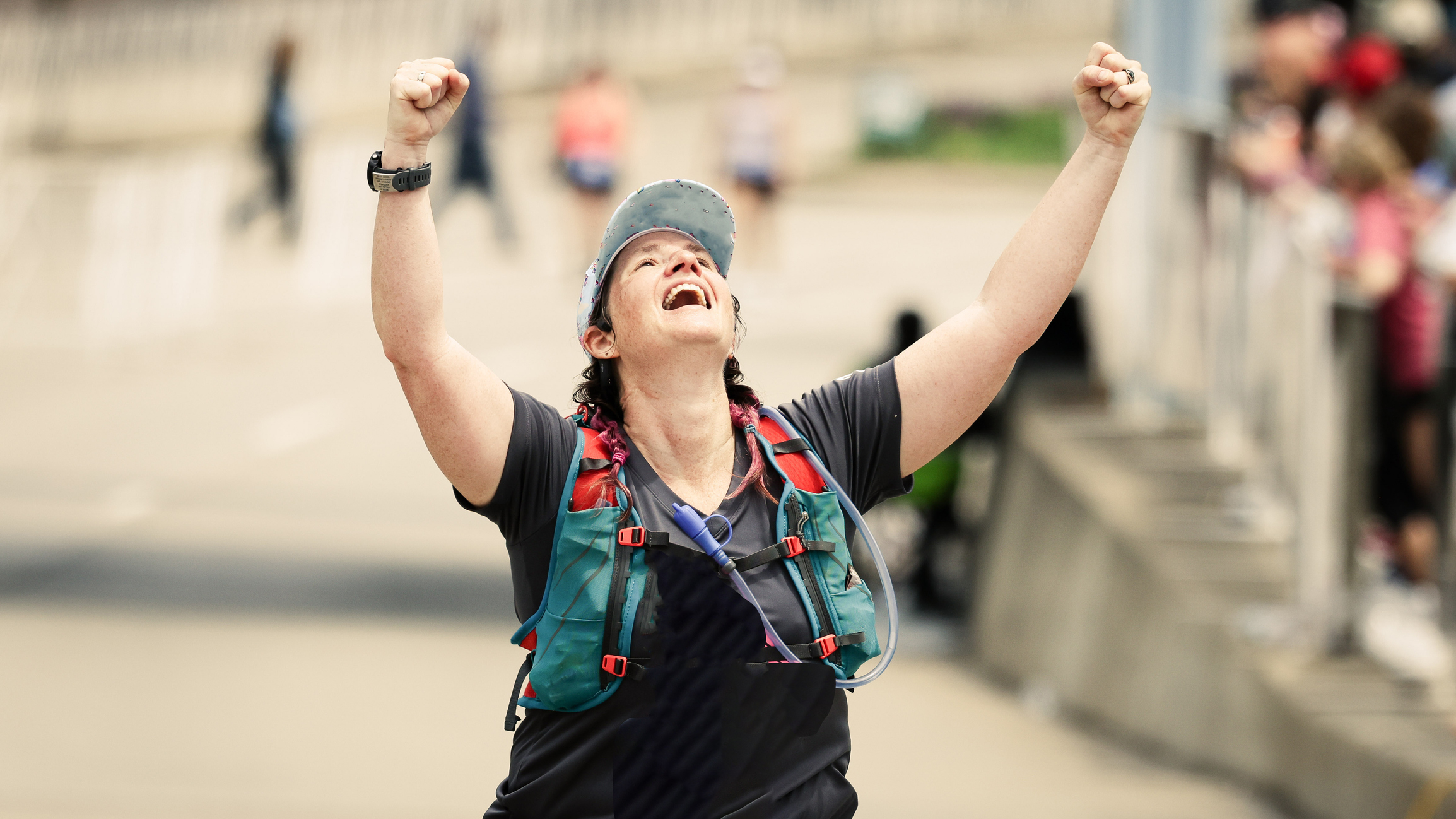 Person celebrating with raised arms, wearing a cap and a backpack