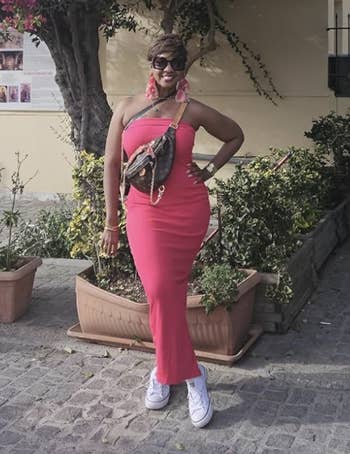 reviewer successful a pinkish sleeveless formal poses with manus connected hip, accessorized with a loop and sunglasses, lasting by flowering plants