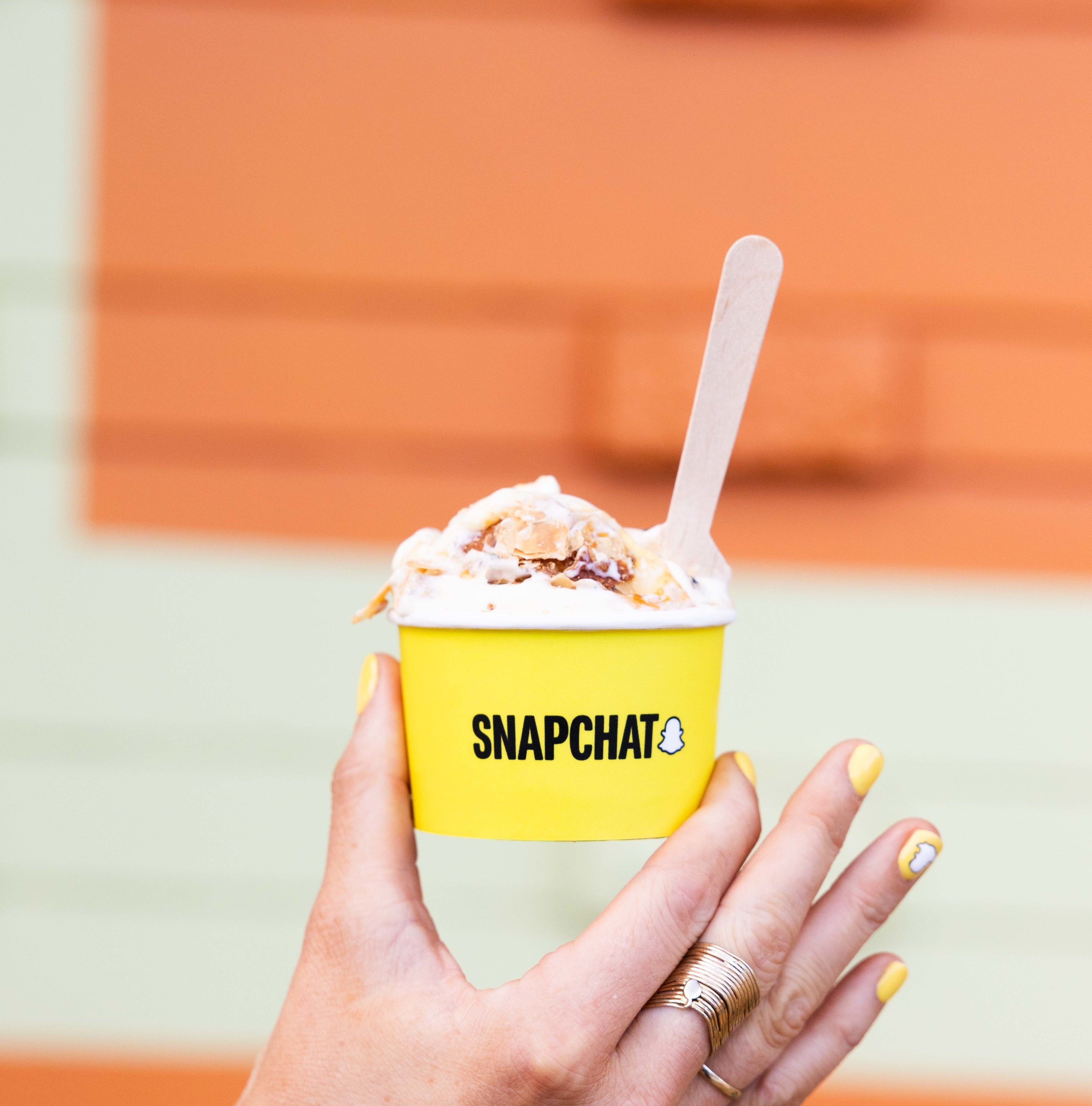 Person holding a Snapchat-branded cup of ice cream with a wooden spoon