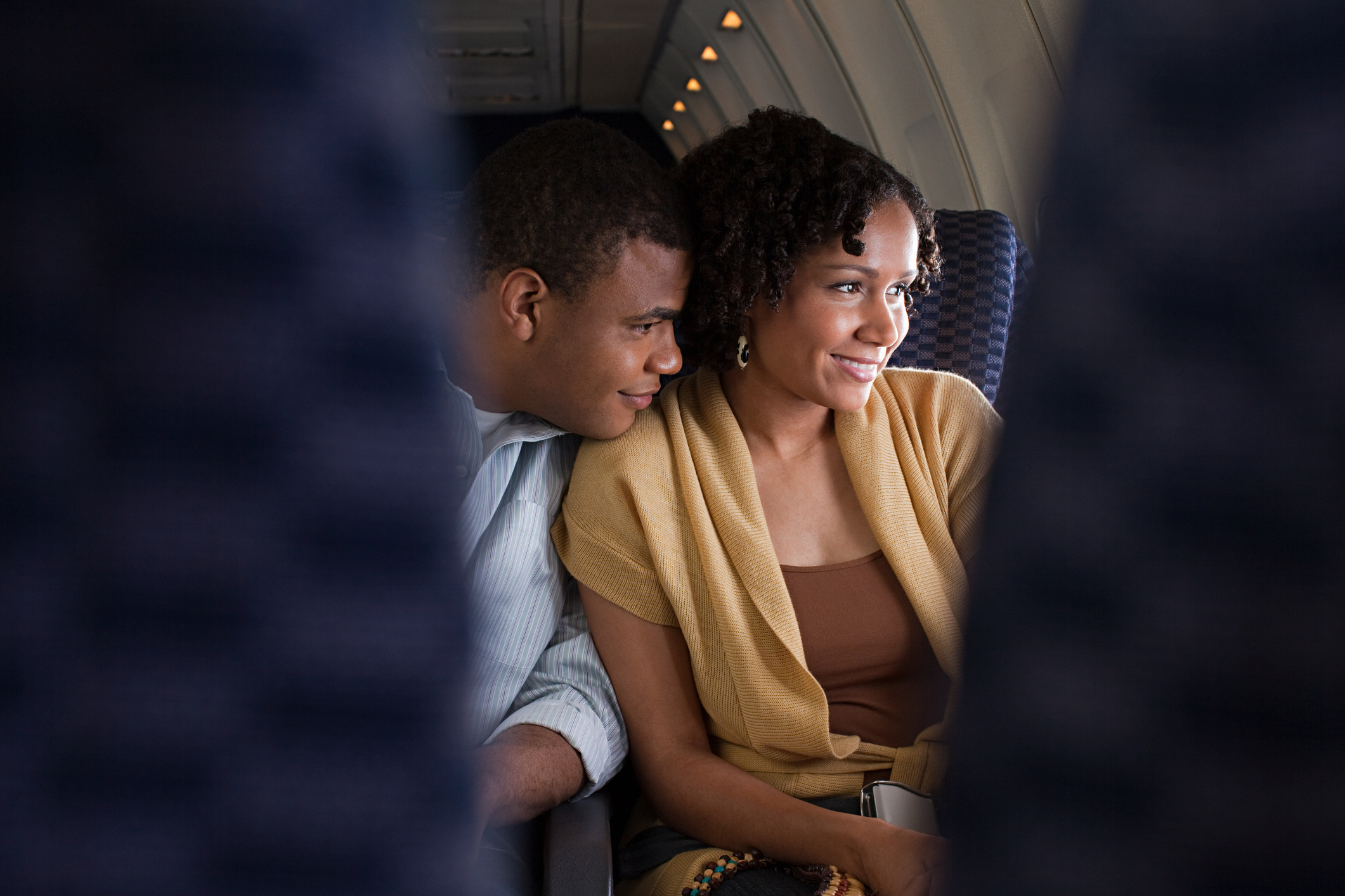 Two people smiling and looking out an airplane window. The image is used to convey a cozy travel experience, related to Tasty category article