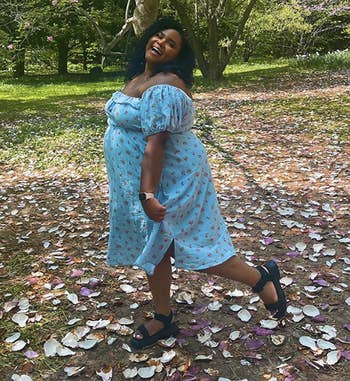 reviewer successful a floral formal stands successful a parkland with fallen petals, smiling with 1 manus connected hip