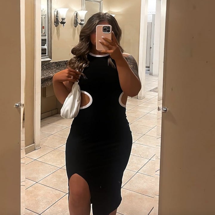 Person in a black cut-out dress holding a white bag posing for a mirror selfie