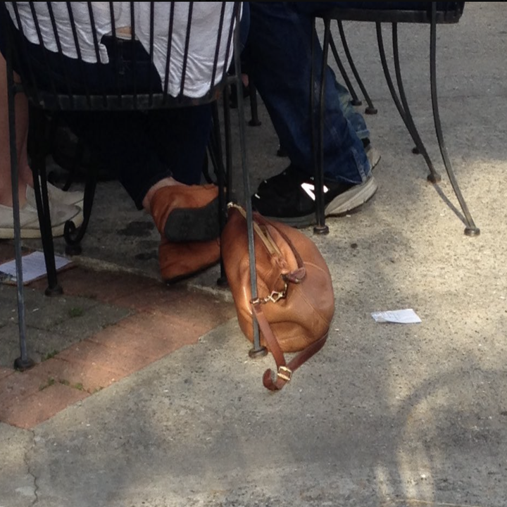 Two people sitting at a table with a dropped brown purse on the ground
