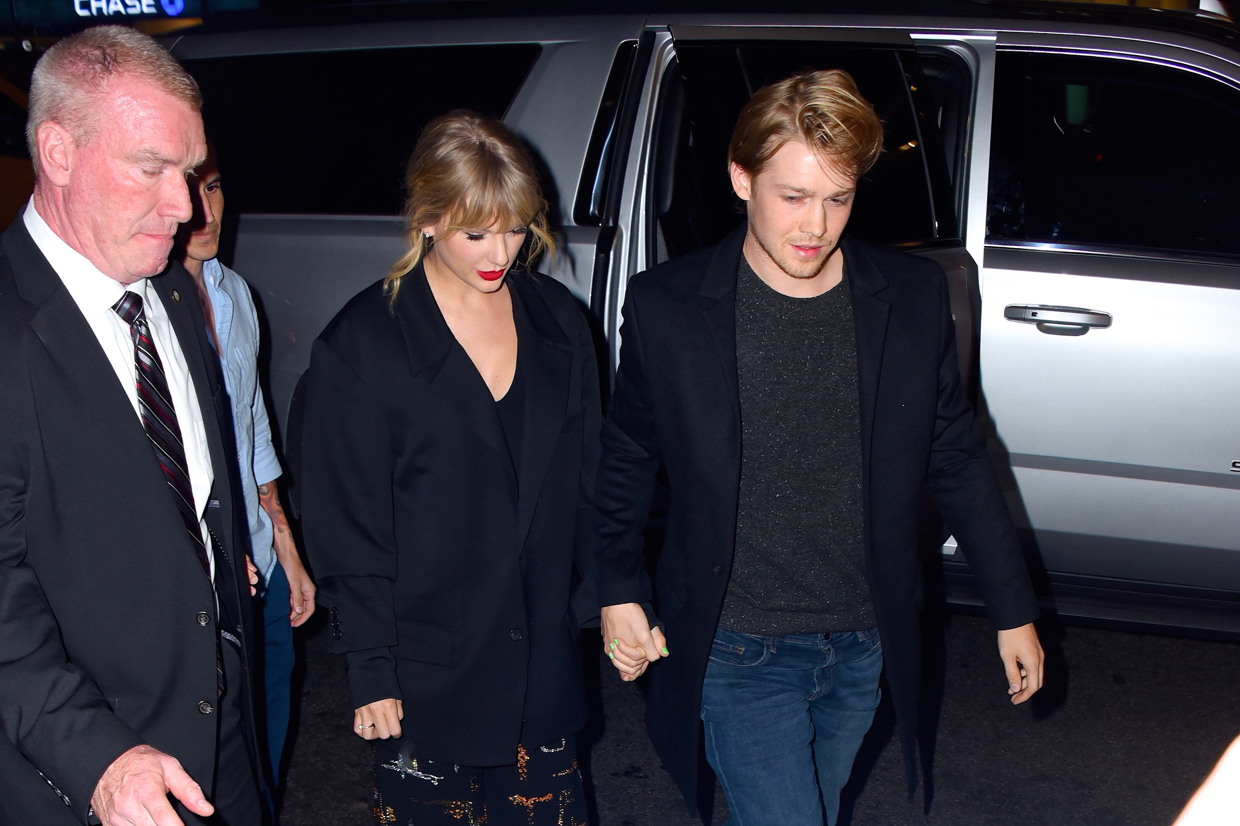Taylor Swift and Joe Alwyn holding hands, exiting vehicle, in elegant attire