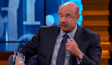 Dr. Phil gesturing while talking, wearing a dark suit on his TV show set