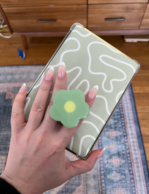 A person holds a phone with a green patterned case and a pop socket accessory