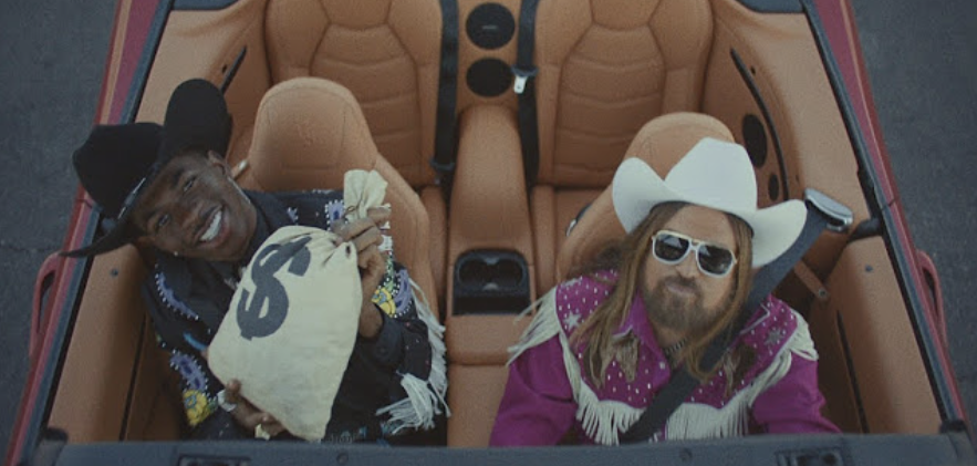 Lil Nas X and Billy Ray Cyrus in cowboy attire, sitting in a convertible, referencing the song &quot;Old Town Road.&quot;