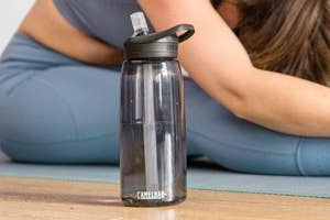 A transparent water bottle with a logo on a yoga mat, beside a person in a resting pose