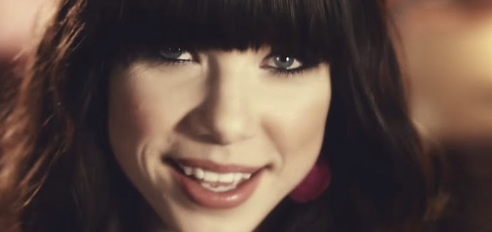 Close-up of Carly Rae Jepsen smiling with bangs and minimal makeup in a music video