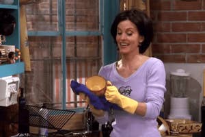Monica Geller from Friends smiling while cleaning a dish, wearing gloves and a casual shirt with a doodle