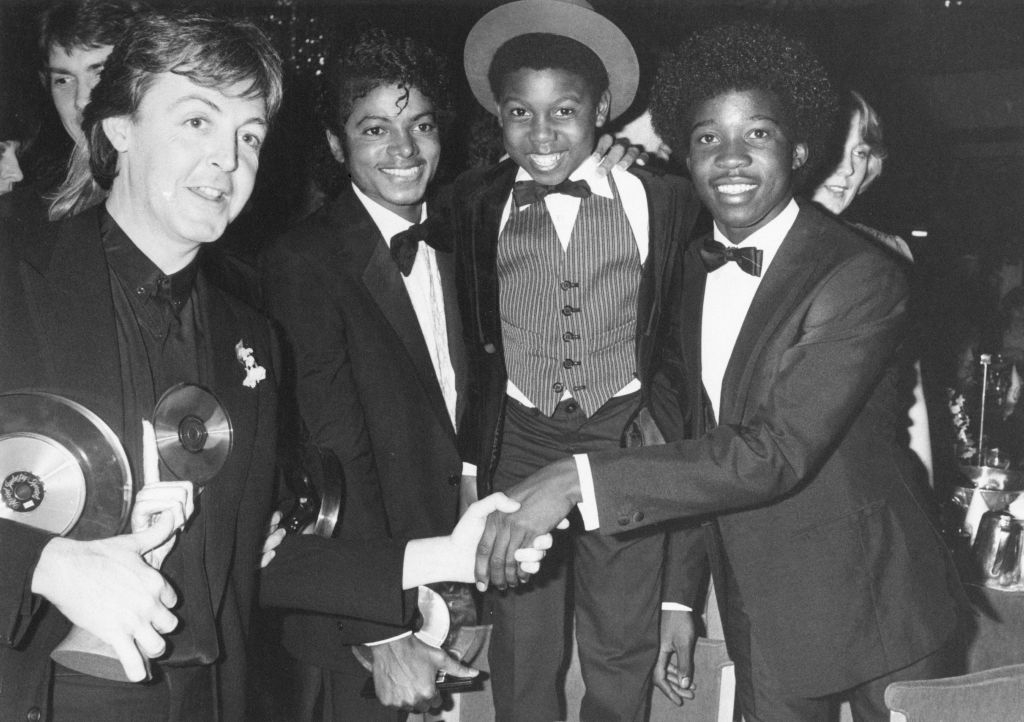 Paul McCartney and Michael Jackson shaking hands, with two young men, all in formal attire at a gala event