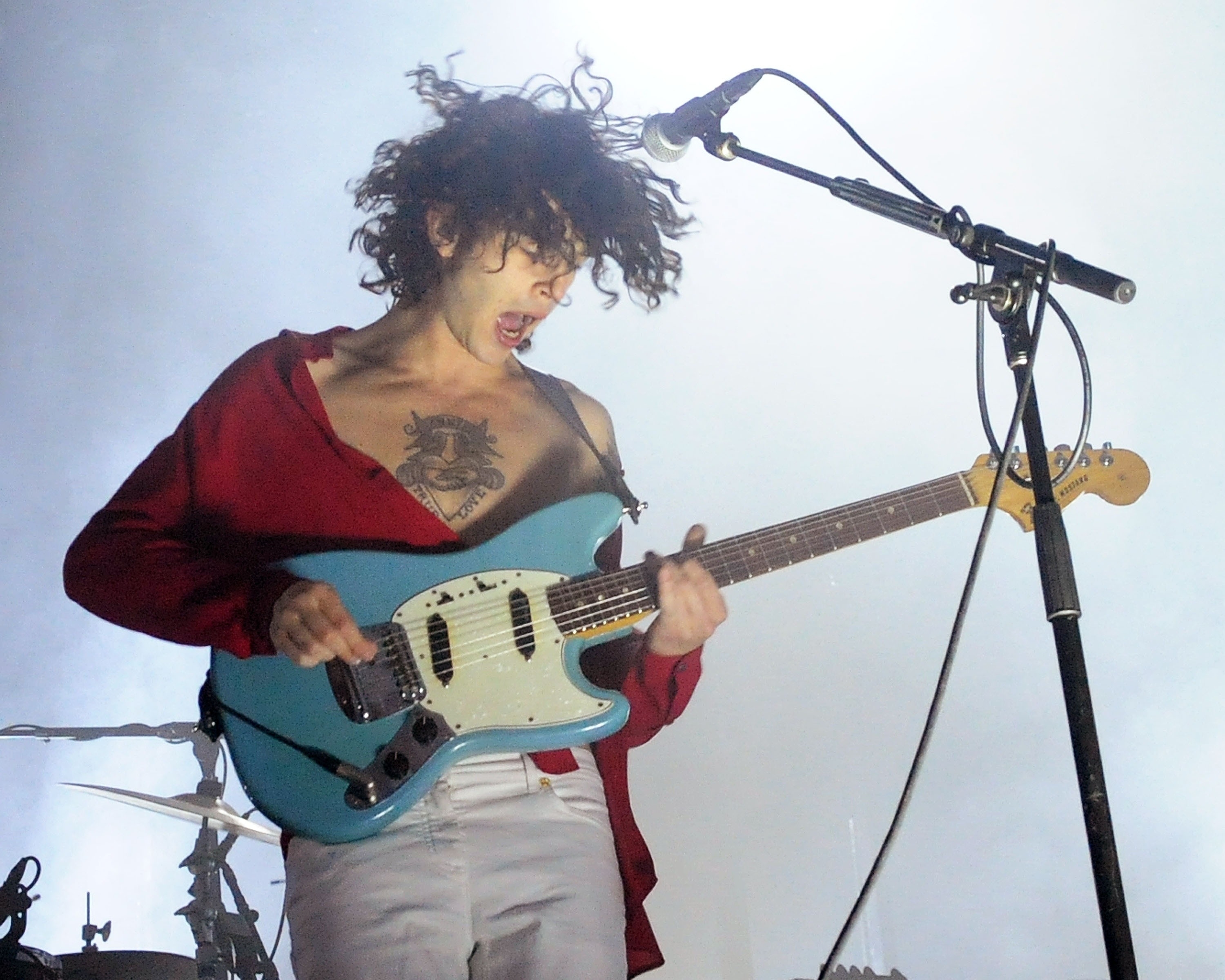 Matty Healy mid-performance playing electric guitar, tattoos visible, casual outfit, focused expression
